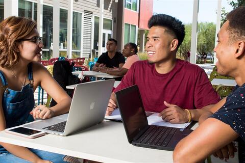 Students sitting at an outdoor table on their laptops